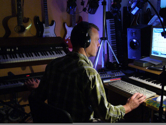Nigel working at a mixing desk in a studio surrounded by guitars and keyboards